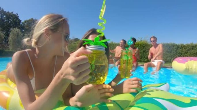 穿着泳装的年轻多民族朋友的真实照片是在五颜六色的充气设备上放松身心，并在阳光明媚的日子里一起在游泳池
