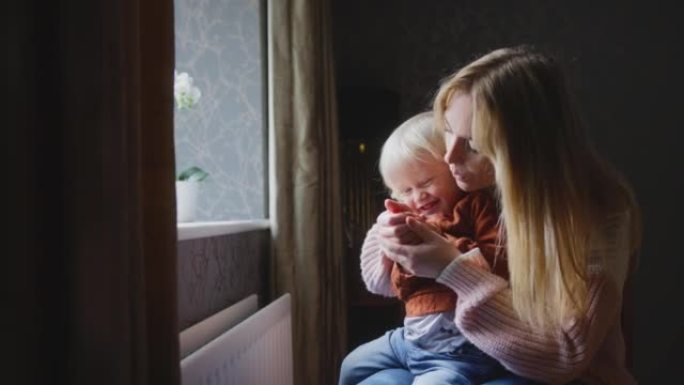 母亲拥抱儿子试图在生活成本能源危机期间在家中通过散热器保暖