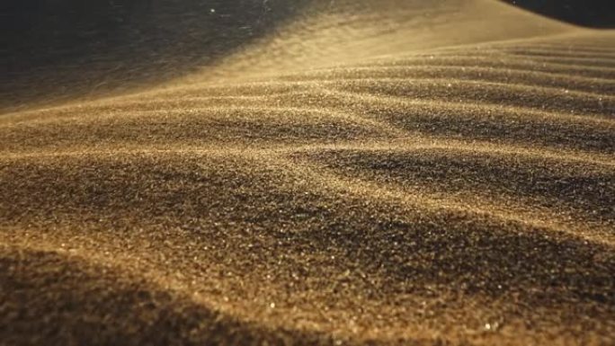 沙漠中的沙尘暴。被风吹走的沙粒的宏观拍摄。相机在夕阳的光线下沿着沙漠中的沙丘表面移动。沙子在风中挥舞