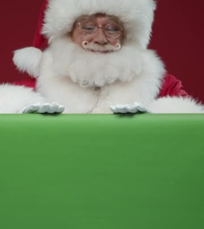 圣诞老人从色度键后面出现在框架中，微笑着抚摸它，然后竖起大拇指，躲在后面