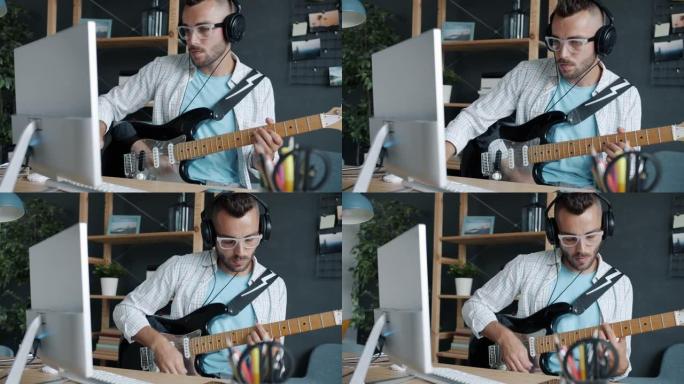 戴着耳机弹吉他在家使用电脑的年轻人的慢动作肖像