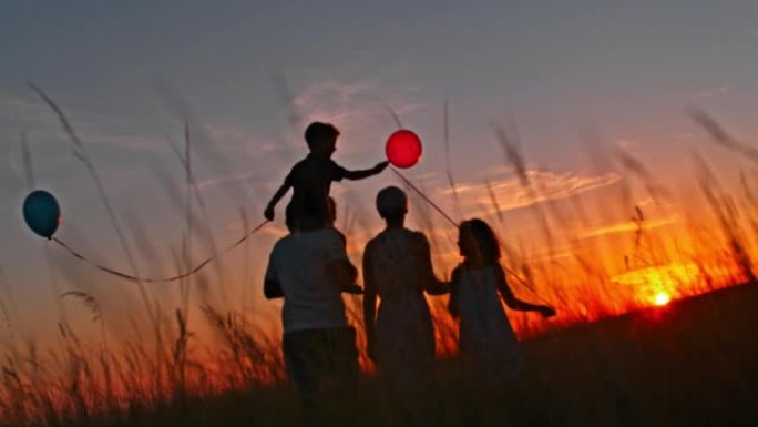 带着两个孩子的SLO MO家庭在日落时在草地上散步