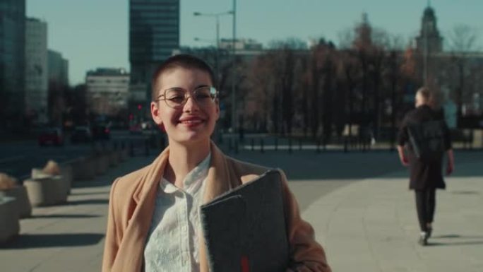 灵感和积极的情绪。年轻快乐聪明的女人带着笔记本电脑走在阳光明媚的城市广场慢动作。