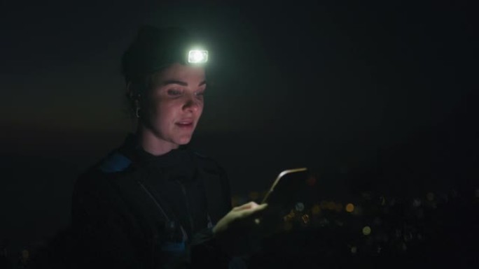 4k视频片段，一名妇女在夜间在户外时戴着头灯并使用手机