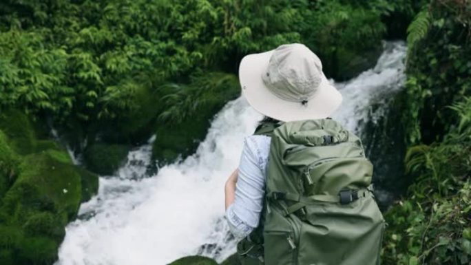 年轻女子站在山上的一条小溪边徒步旅行