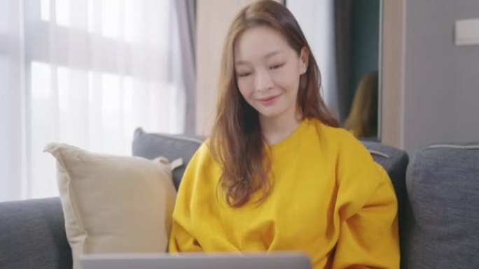 美丽的亚洲年轻女子年龄36岁穿着彩色黄色衬衫在家工作的笔记本电脑。成人在线学习概念。与阿尔法香奈儿。