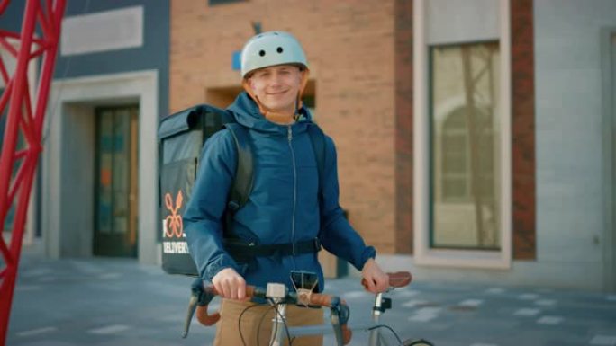 穿着保暖背包和安全帽的英俊快乐送餐男子站在时尚的现代市区的自行车旁边。微笑的快递员递送餐厅订单的肖像