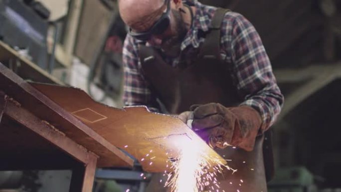 男性铁匠戴着安全眼镜，使用等离子切割机从锻造的钣金切割形状