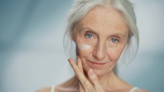 美丽的高级女人轻轻涂抹面霜的肖像。老年女士用天然抗衰老化妆品使皮肤柔软、光滑、无皱纹。美容护肤、化妆