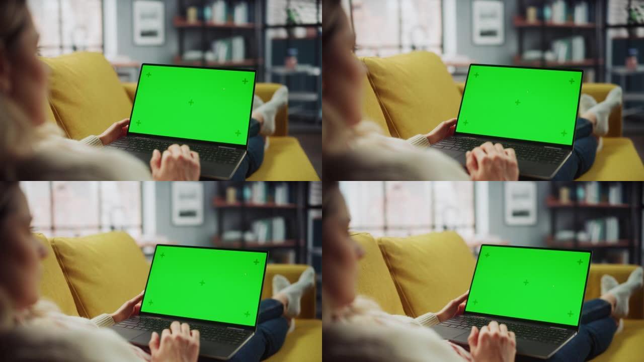 美丽的高加索专家躺在沙发上，在家里的客厅用绿屏模拟显示笔记本电脑工作。自由女性在社交网络上通过互联网
