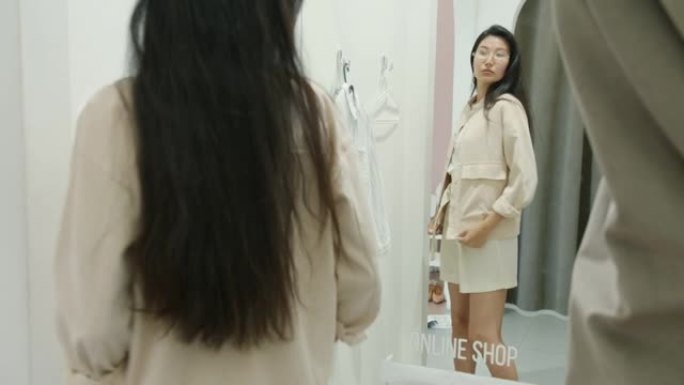 快乐的年轻亚洲女性在试衣间试穿衣服，独自购买时尚服装