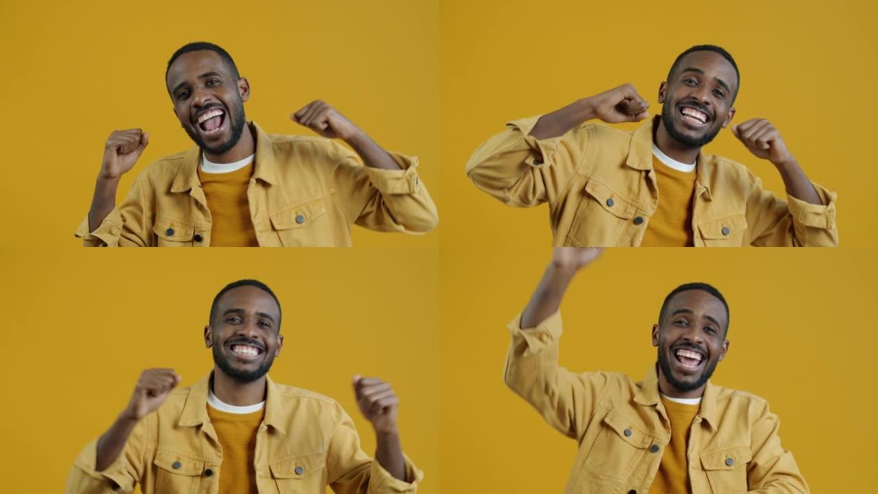 快乐的非洲裔美国人微笑着看着黄色背景上的相机跳舞的慢动作肖像