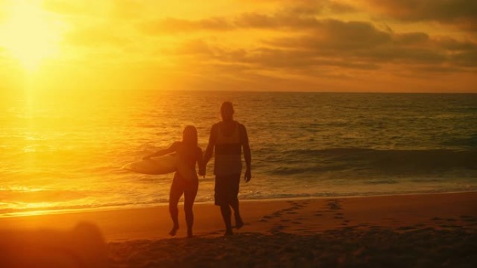 美丽的日落女子手持冲浪板从海边散步时，异性夫妇牵手