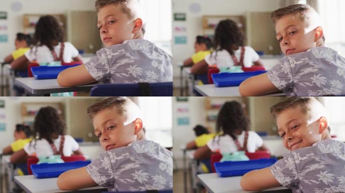 快乐的高加索男生的肖像坐在教室里，做笔记，看着相机