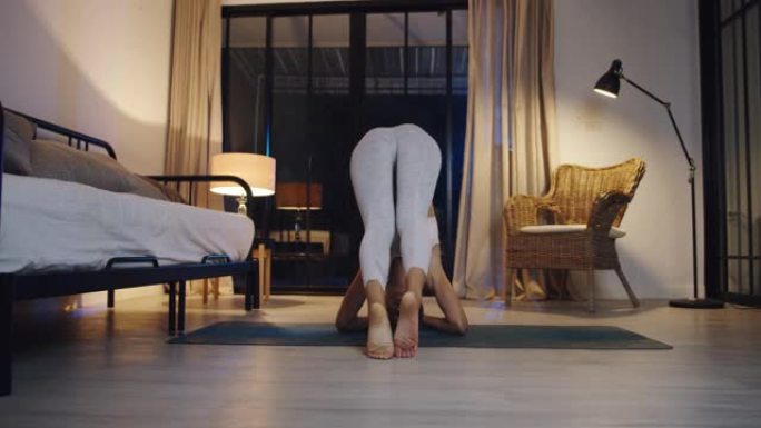 穿着运动服的年轻亚洲女士晚上在家客厅做瑜伽锻炼。