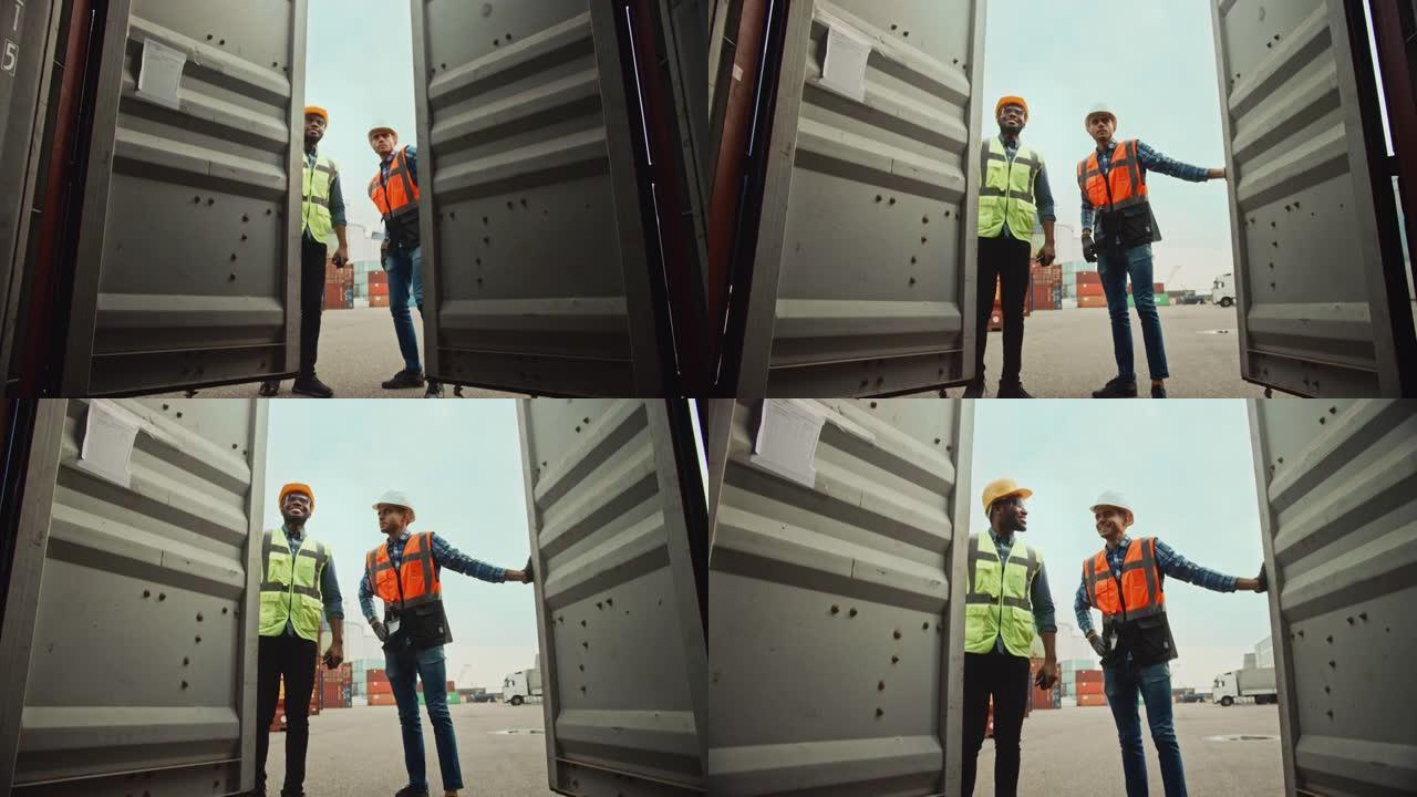 英俊的工业工程师和非裔美国人主管，戴着安全帽和安全背心，在物流码头打开一个货运集装箱。打开门时，两个