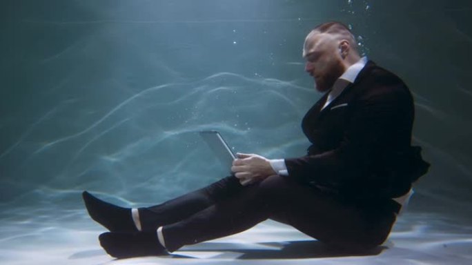 电影在水侧视图下，年轻快乐的工作狂商人穿着黑色西装，使用笔记本电脑慢动作。