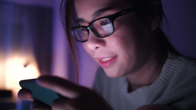 女人晚上在卧室的床上使用智能手机上网和社交媒体
