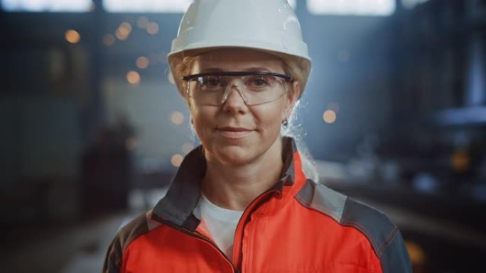 钢铁厂中一位专业的重工业工程师/工人穿着制服，戴着眼镜和安全帽的肖像。美丽的女性工业专家站在金属建筑