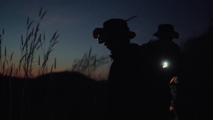 日落时爬山时使用手机手电筒的男性游客的剪影