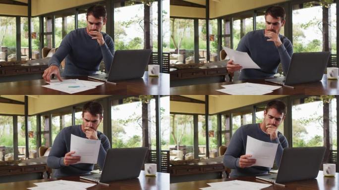 体贴的白人男子在度假屋阅读文件和使用笔记本电脑