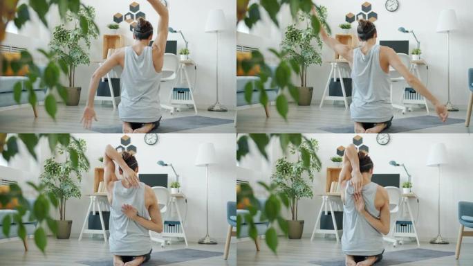 灵活的男运动员伸展手臂在公寓里做瑜伽的后视图