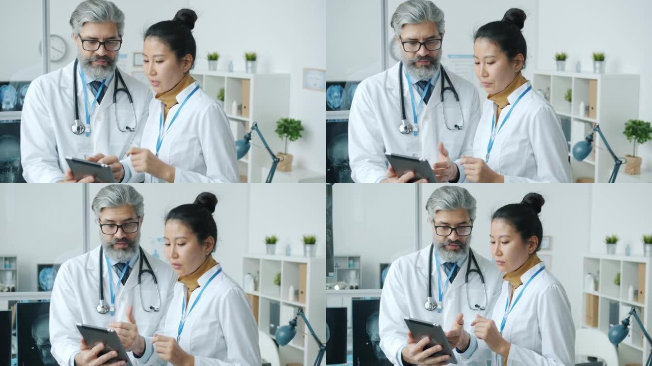 医生高加索男人和亚洲女人在医院办公室里聊天和看着笔记本电脑屏幕