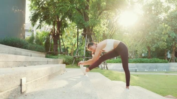 美丽的年轻亚洲运动员女士在日落时分在城市公园环境中跑步后锻炼身体热身。