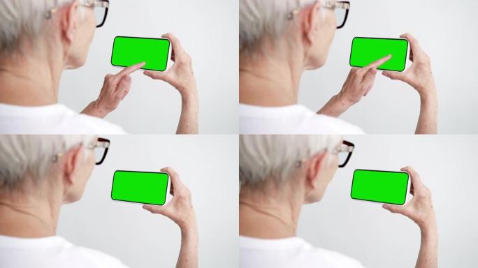 老人触摸和滑动屏幕智能手机与绿色色度键特写。50多岁的女性手持手机点击模型。概念观看和展示画廊社交媒