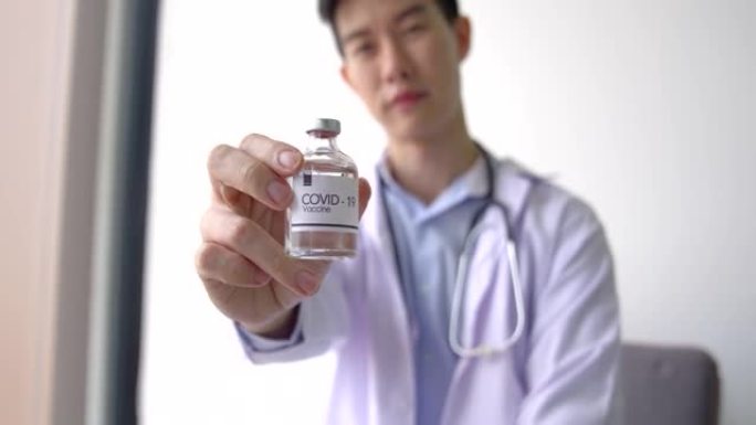 年轻的男性医生拿着一个新型冠状病毒肺炎的疫苗瓶，它传达了希望有一个疫苗来帮助预防流行病。