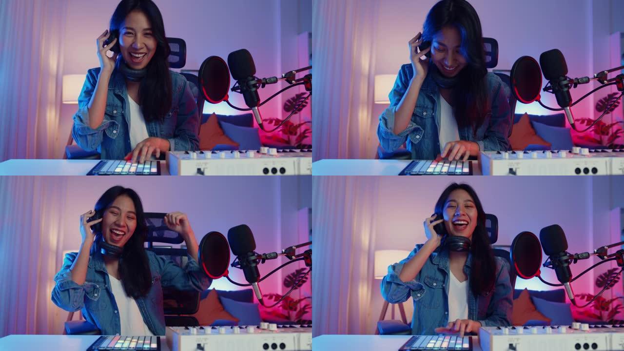 快乐亚洲女孩dj播放启动板合成器键盘混音器戴着耳机和表演音乐在线直播晚上在客厅家庭工作室与观众交谈。