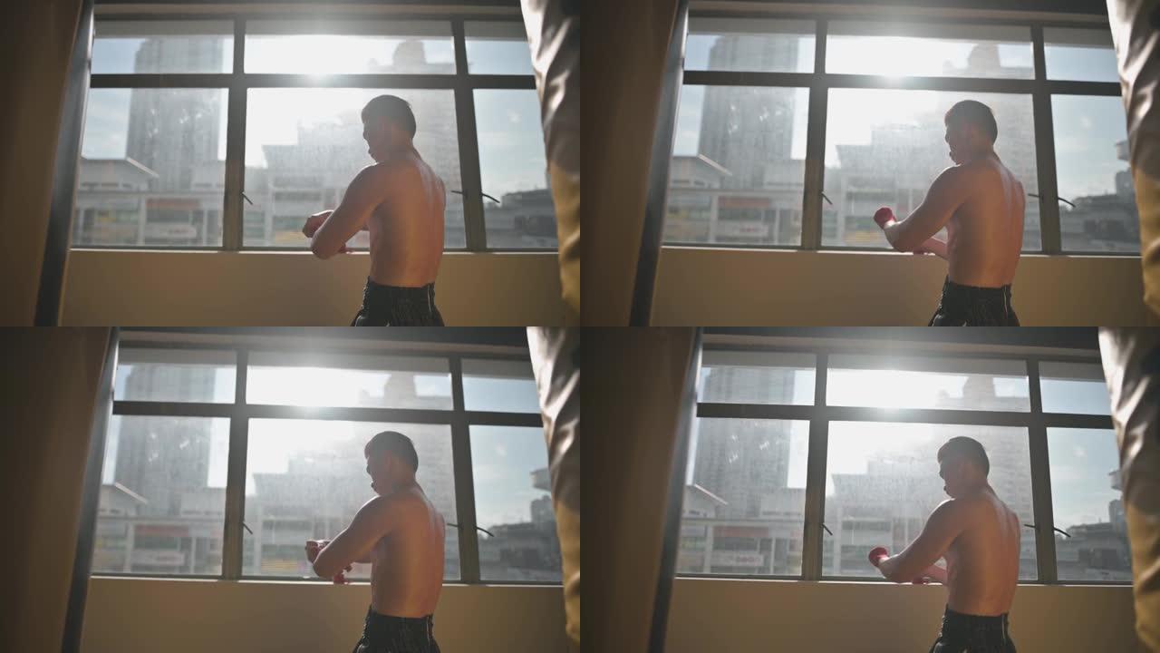 亚洲中国泰拳拳击手系好绷带内运动手套，准备晚上在窗户附近进行拳击训练