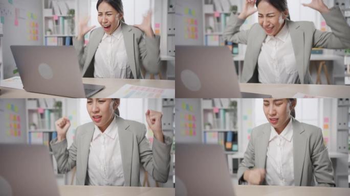 年轻的亚洲女商人坐在办公桌上疯狂地工作，压力过大，愤怒的大规模工作在办公室尖叫。