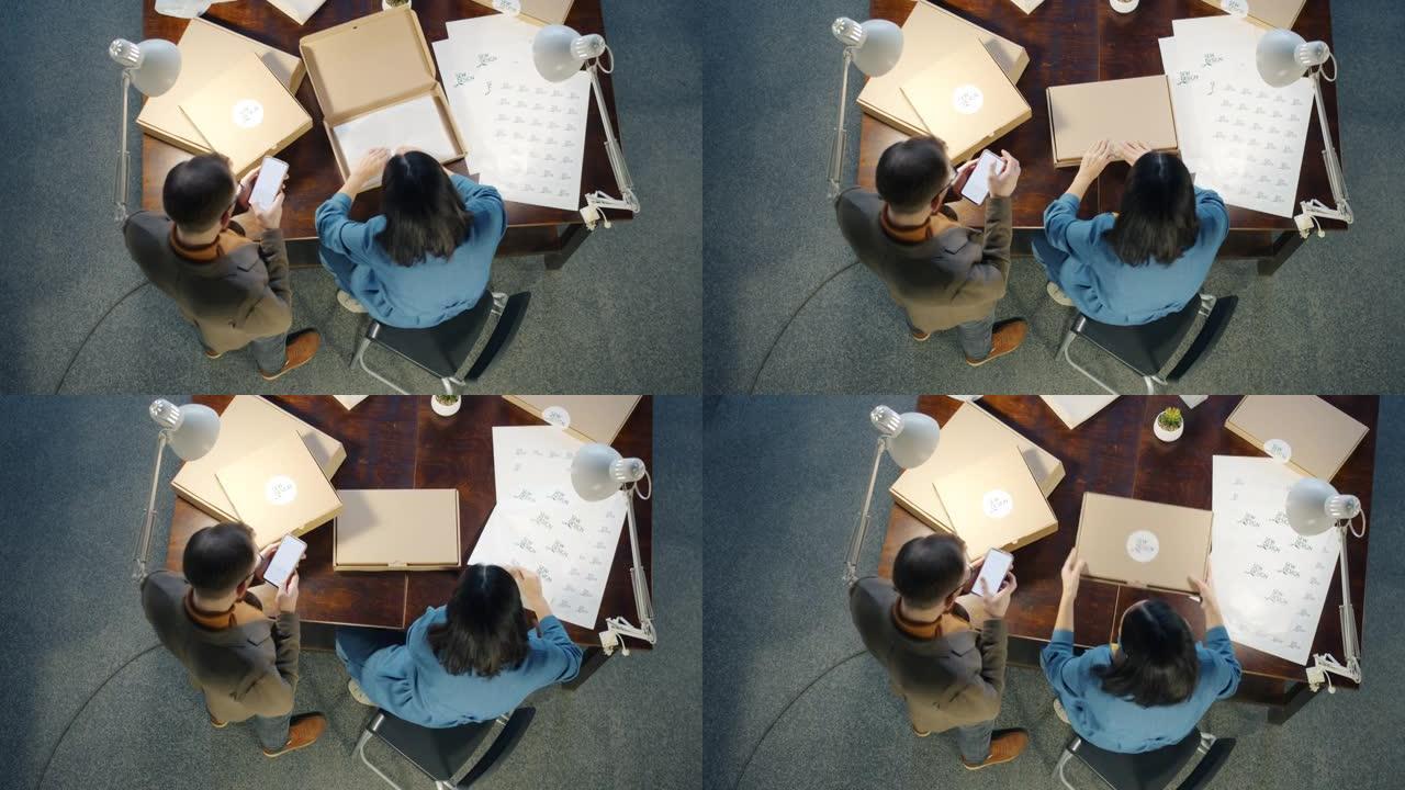 在工作室工作的纸板箱中包装手工服装的商业伙伴的俯视图