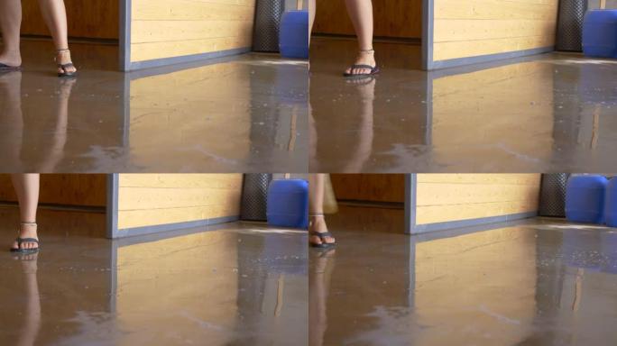 低角度: 面目全非的女人用稻草扫帚扫过被水淹没的地板。