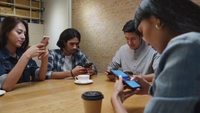 一群快乐的年轻亚洲朋友玩得开心，一起坐在咖啡馆餐厅使用智能手机。