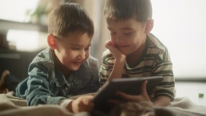 两个亚洲男性孩子的肖像在周末在他们的房间里使用数字平板电脑。两个可爱的兄弟姐妹在线观看教育内容，分享