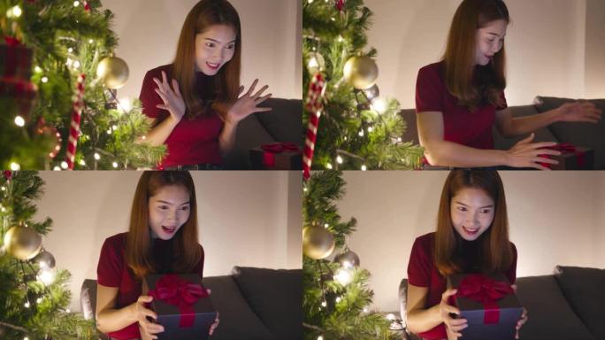 年轻的亚洲女性使用平板电脑视频通话与圣诞礼物盒子的情侣交谈，圣诞树装饰着家里客厅的装饰品。