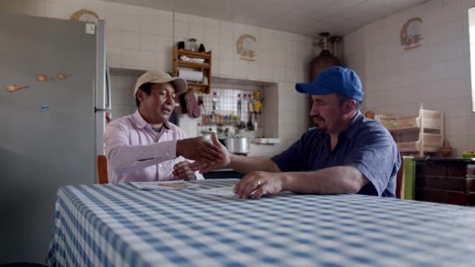 男性农民在讨论生意并坐在质朴的厨房里用握手看文件后达成交易