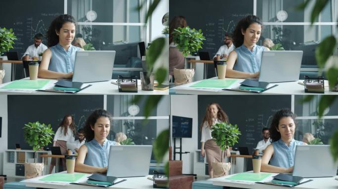 同事在共享办公室的背景下工作时，开朗的年轻女子使用笔记本电脑打字