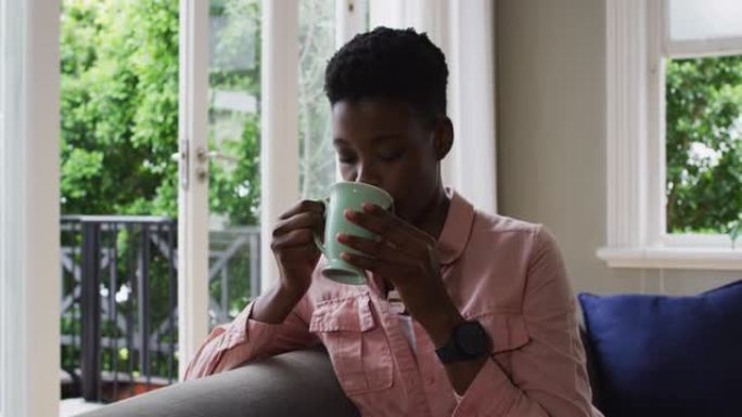 非裔美国妇女坐在家里的沙发上喝咖啡