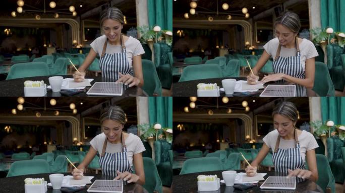餐厅的快乐女业务经理使用平板电脑和文档做书籍
