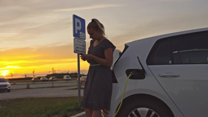 SLO MO女人在日落时为汽车充电时使用智能手机