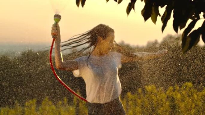 超级SLO MO年轻女子开心地用花园水管喷水
