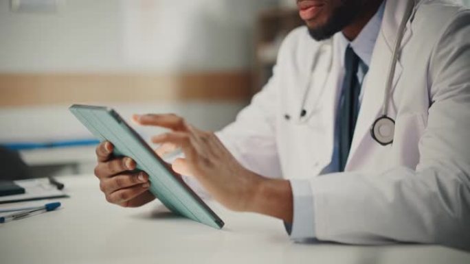 近距离观察穿着白大褂的非裔美国男医生在办公室用平板电脑工作。医疗保健专业人员处理测试结果，病人治疗计