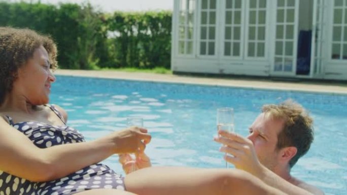 暑假里成熟的女人在室外游泳池边缘晒日光浴，男人带来了一杯香槟来庆祝 -- 慢动作拍摄