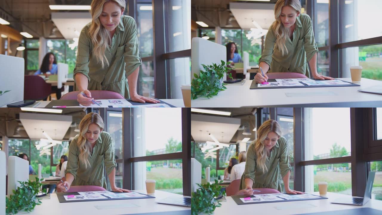 相机向后拉，显示成熟的女商人站在办公室的办公桌前，批准布局或样张并喝咖啡-慢动作拍摄
