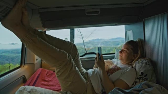 金发碧眼的女人正躺在她的面包车里，伸着腿，用她的智能手机