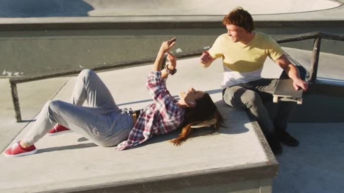 快乐的高加索男女朋友在滑板场使用智能手机
