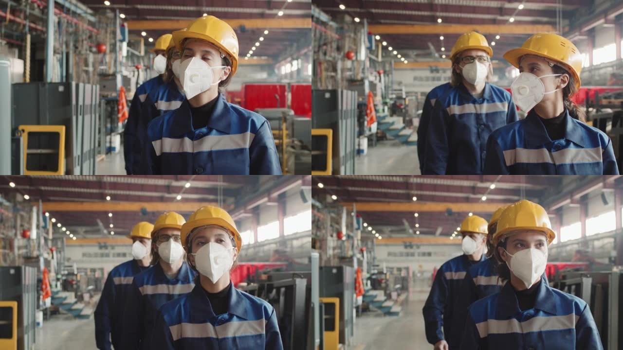 女主管戴着口罩的工人走过工厂